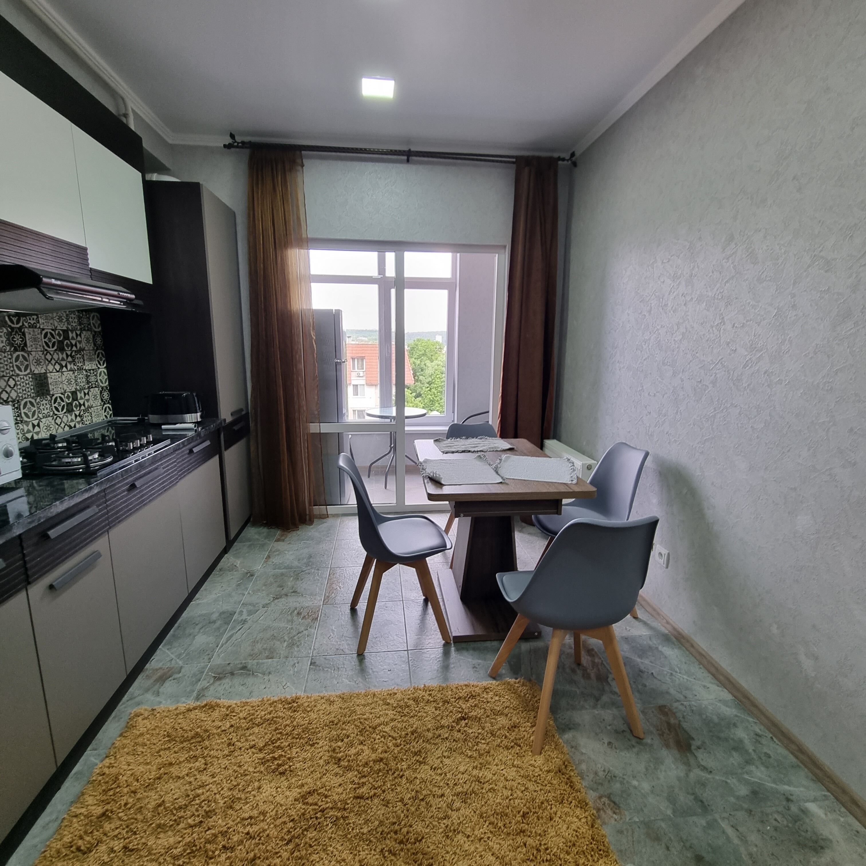 A compact kitchen with modern appliances, a dining area with a table and chairs, and a view through a window.