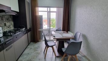 A compact kitchen with modern appliances, a dining area with a table and chairs, and a view through a window.