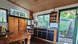 A rustic kitchen with wooden cabinets, a large wooden table, and a window overlooking a garden.