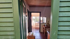 A narrow hallway with green walls and wooden flooring leading to a room with a table and chairs.