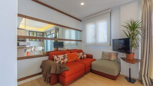 A modern living room with a red sofa, a small table with a plant, a TV, and a large mirror reflecting the kitchen area. - Penthouse Central: swimming pool terrace parking parking sea view (Tarifa)