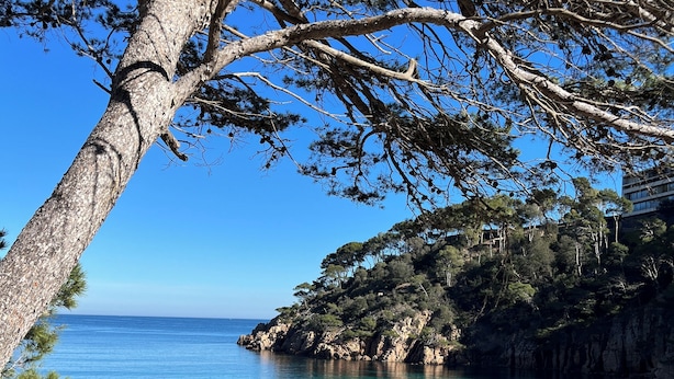 A coastal landscape with clear turquoise waters, rocky cliffs, and a sandy beach.