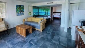 A room with a sofa, a small wooden table, a bed, and a kitchen area. - Jacuzzi Suite Overlooking the Sea @Islamorada - Iguana Suite (Islamorada)