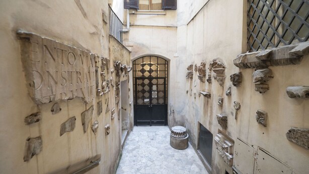 A narrow alleyway with a black gate, stone wall decorations, and a small round object on the ground. - Elegant Roman Retreat by Campo de Fiori (Roma)