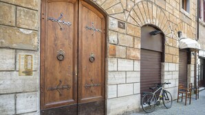 A building with two wooden doors, a bicycle, and a chair outside. - Elegant Roman Retreat by Campo de Fiori (Roma)