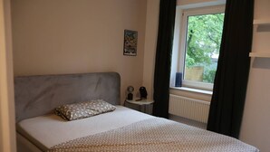 A bedroom with a bed, a nightstand, a window with curtains, and a poster on the wall.