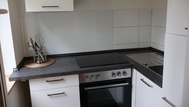 A compact kitchen with a stove, oven, and sink. There are white cabinets and a black countertop.