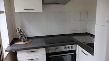 Een koelkast, een oven, een kookplaat, kookgerei, borden en bestek