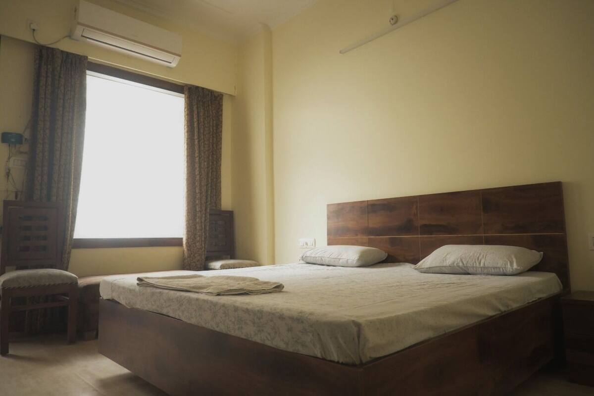 Un dormitorio con una cama grande, una mesita de noche, una silla, un cabecero de madera y una ventana con cortinas.