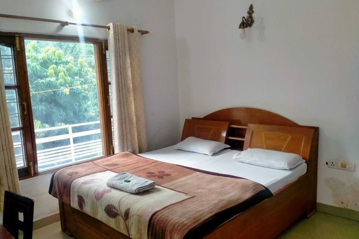 Una cama individual con cabecera de madera, una ventana con cortinas y una lámpara de pared pequeña.