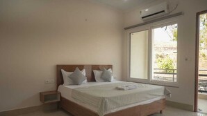 A bedroom with a wooden bed, a nightstand, a large window, and an air conditioning unit. - Mount Valley Mama Cottage (Rishikesh)