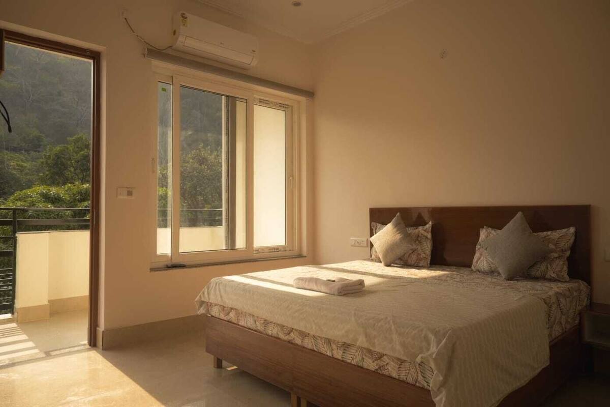Un dormitorio con una cama grande, un balcón con vistas a zonas verdes y un equipo de aire acondicionado.