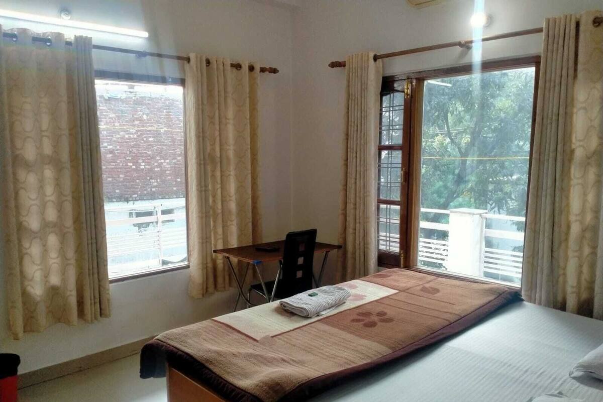 Un dormitorio con cama, escritorio y dos ventanas con cortinas.