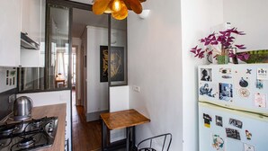 Una cocina compacta con estufa a gas, una mesa de madera y una lámpara de techo original.