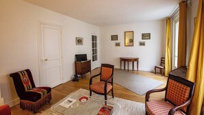 A living room with a red armchair, a wooden chair, a small table, and a television on a wooden stand.