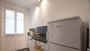 A modern kitchen with white cabinets, a double-door refrigerator, a microwave, and two stools.
