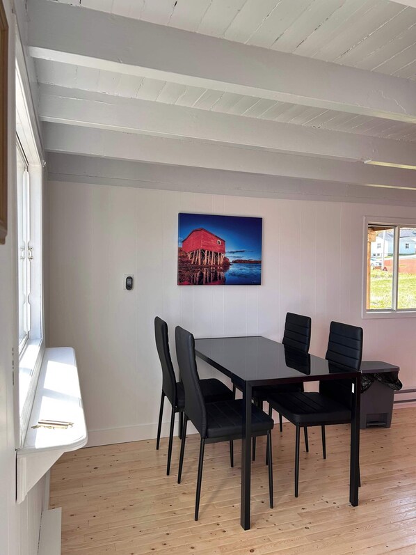 Un coin repas avec une table et des chaises, un tableau accroché au mur et une fenêtre.