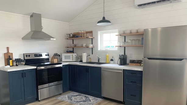 A modern kitchen with a stainless steel refrigerator, a built-in oven, a microwave, and a sink. - Spiller's Cottage (Twillingate)