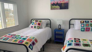 A bedroom with two beds, a nightstand, a lamp, and a painting on the wall. - Spiller's Cottage (Twillingate)