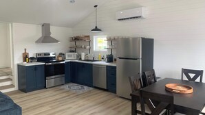 A modern kitchen with a built-in oven, microwave, and refrigerator, wooden flooring, and a dining area with a table and chairs. - Spiller's Cottage (Twillingate)