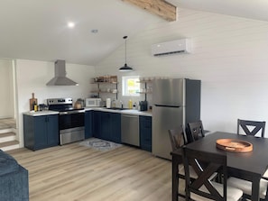 A modern kitchen with a built-in oven, microwave, and refrigerator, wooden flooring, and a dining area with a table and chairs. - Spiller's Cottage (Twillingate)
