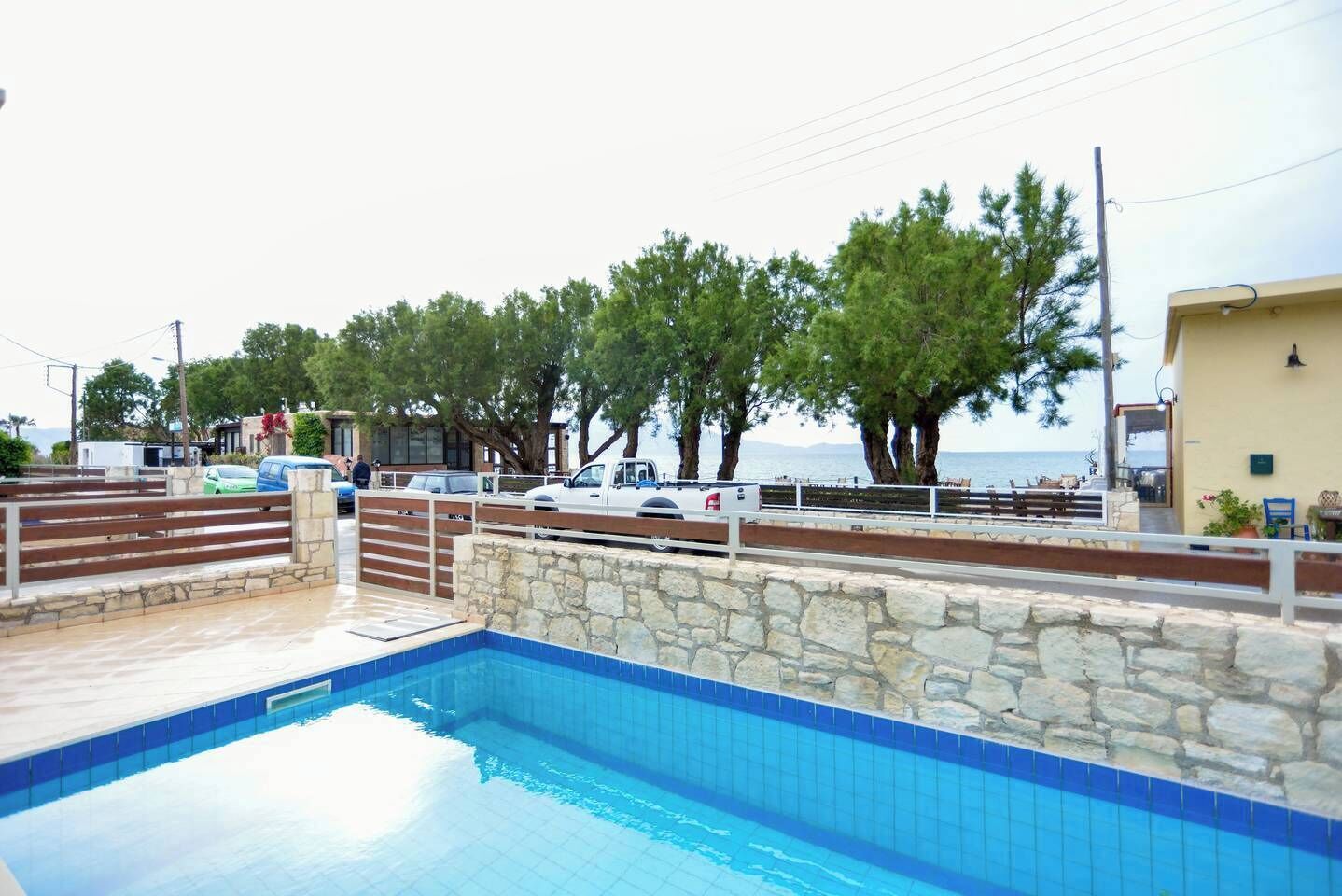 A swimming pool with stone walls, a wooden deck, and a view of the sea.
