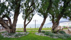 A coastal outdoor seating area with a view of the sea, surrounded by large trees and a well-maintained lawn. - Villa Nopigia Mare, Kissamos Chania (Chania)