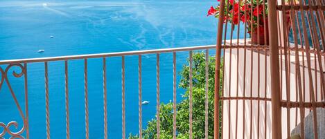 A balcony with a view of the sea, a wicker chair, and red flowers.