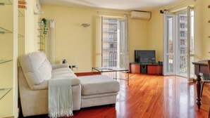 A living room with a sofa, a TV, and a balcony door. - Delightful 2BR flat near Navigli (Milan)