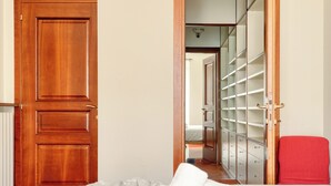A bedroom with a wooden door, a red chair, and a walk-in closet with shelves. - Delightful 2BR flat near Navigli (Milan)