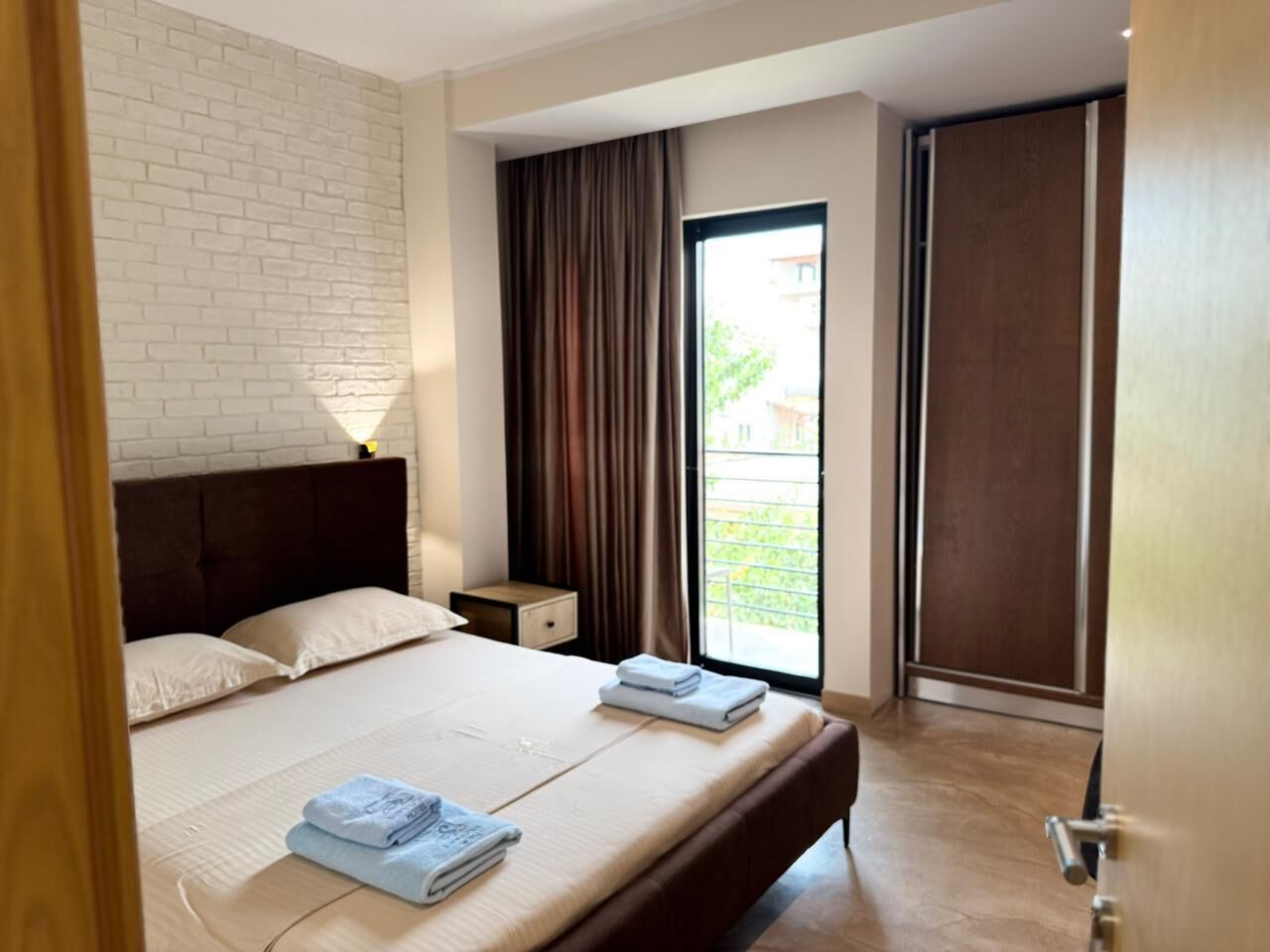 A hotel room with a bed, a nightstand, a window with curtains, and a sliding door.