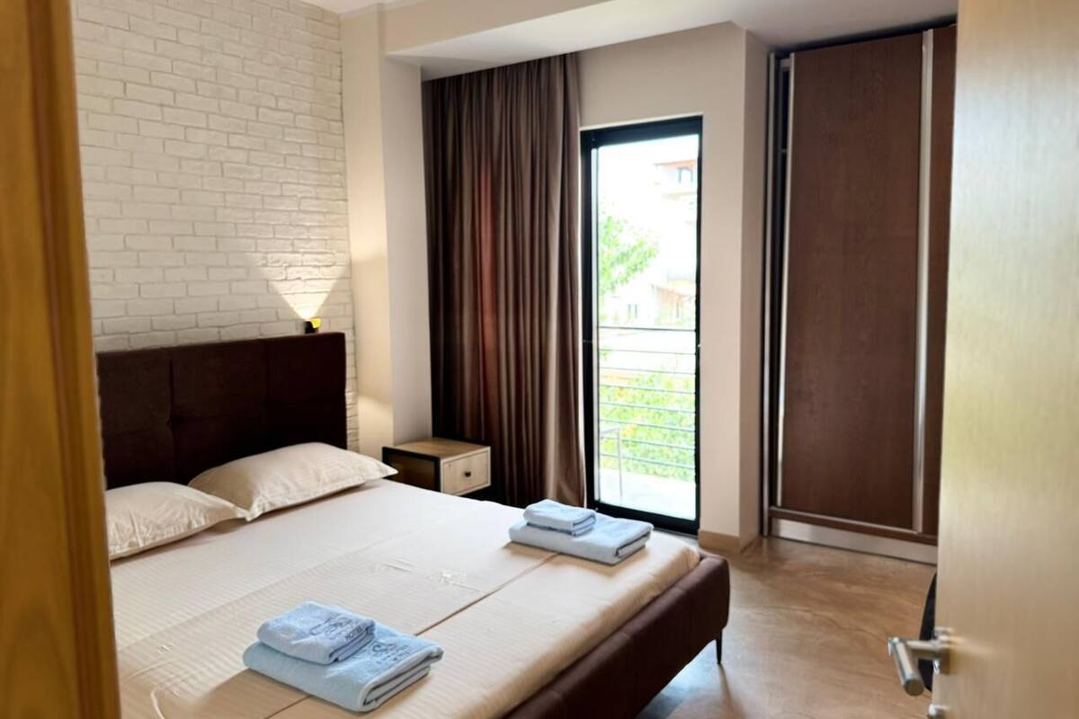 A hotel room with a bed, a nightstand, a window with curtains, and a sliding door.