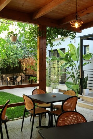 An outdoor patio with a table and chairs, surrounded by greenery and a brick wall. - Ritson Hotel  (Qender Vlore)