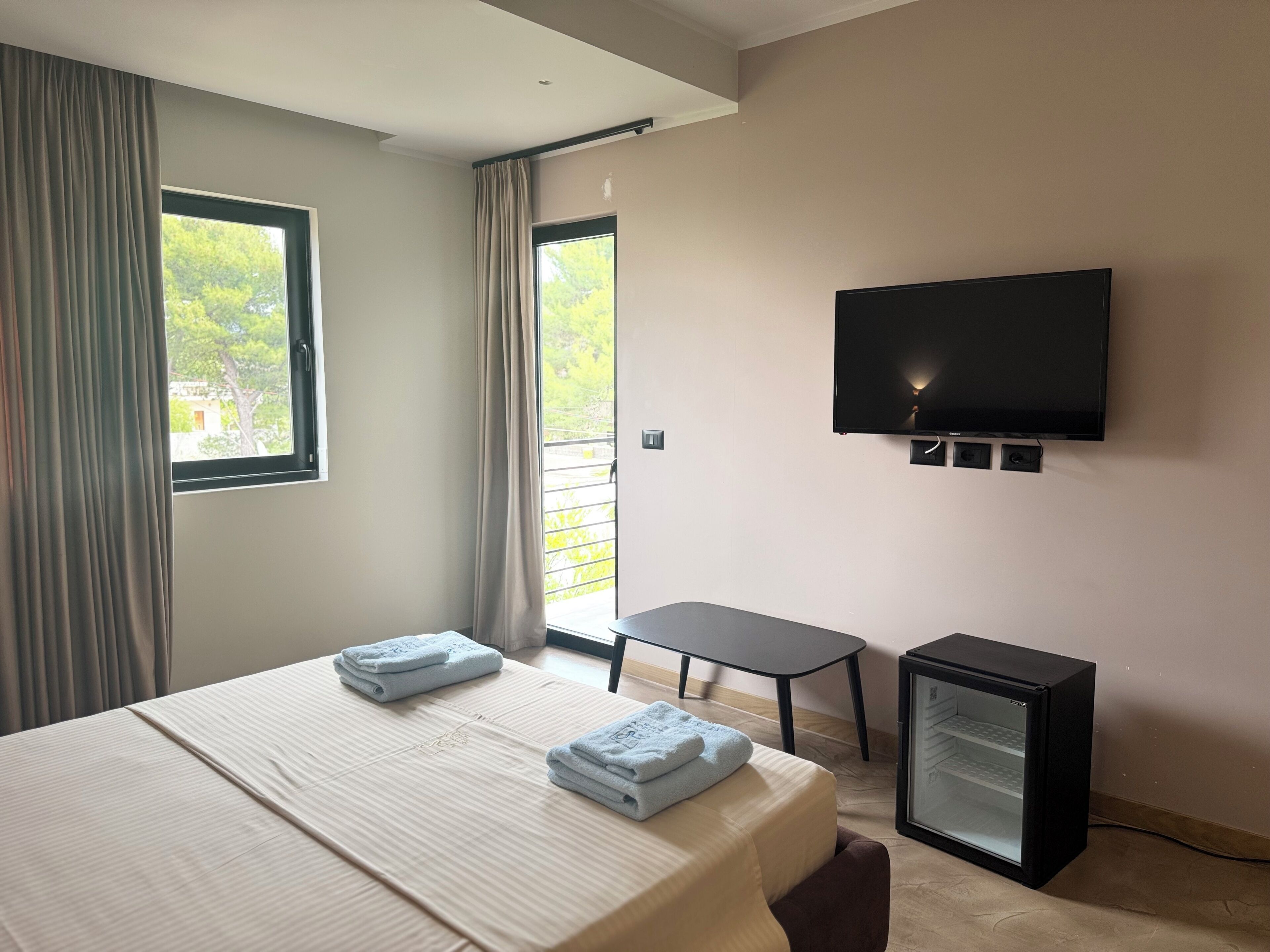 A hotel room with a bed, a TV, a small table, and a refrigerator.