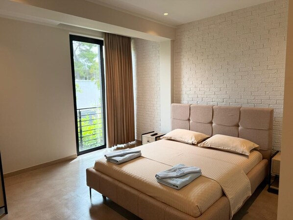 A modern hotel room with a large bed, a nightstand, a window with curtains, and a brick-patterned wall. - Ritson Hotel  (Qender Vlore)