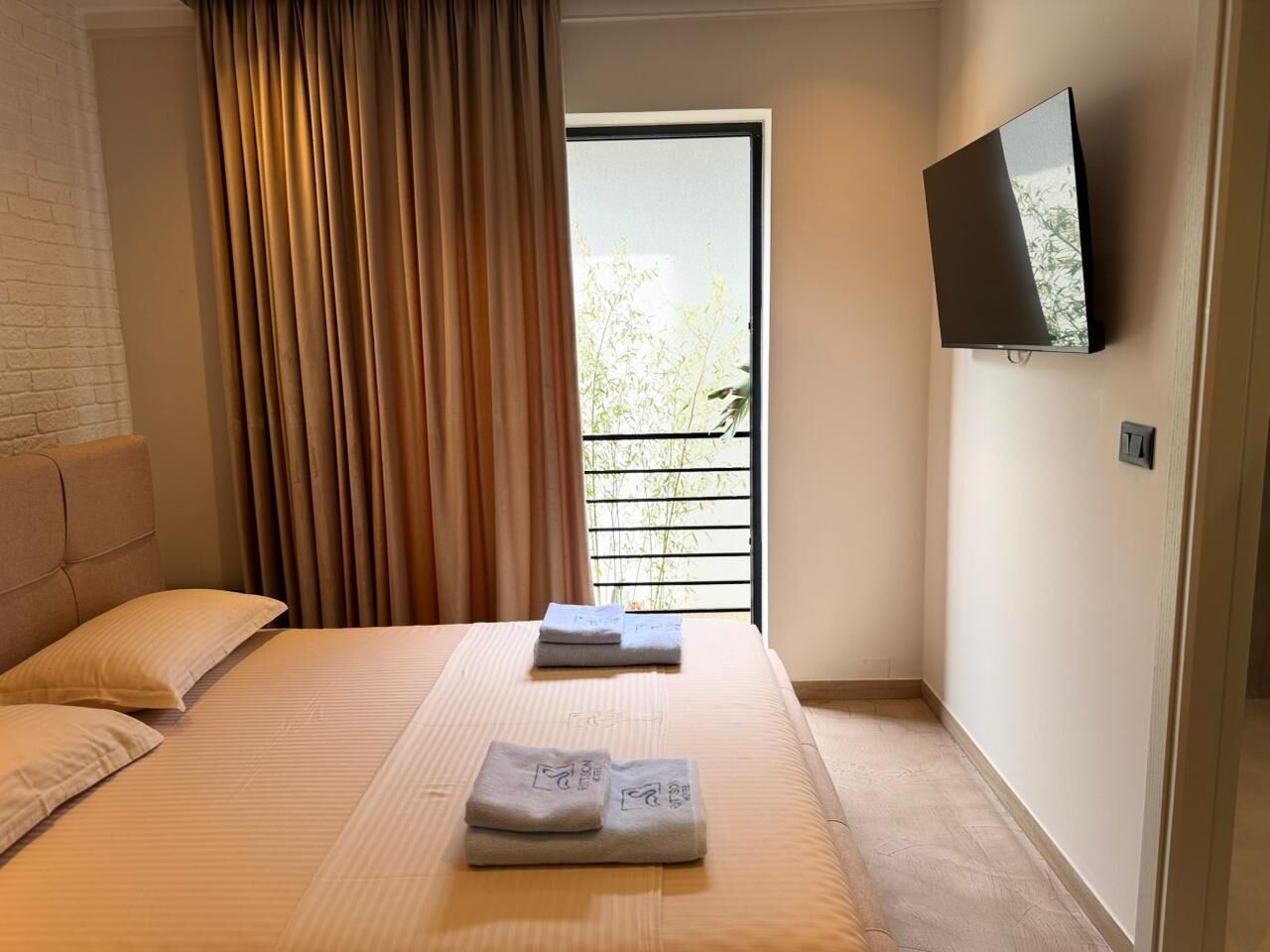 A hotel room with a bed, a TV mounted on the wall, and a window with curtains.