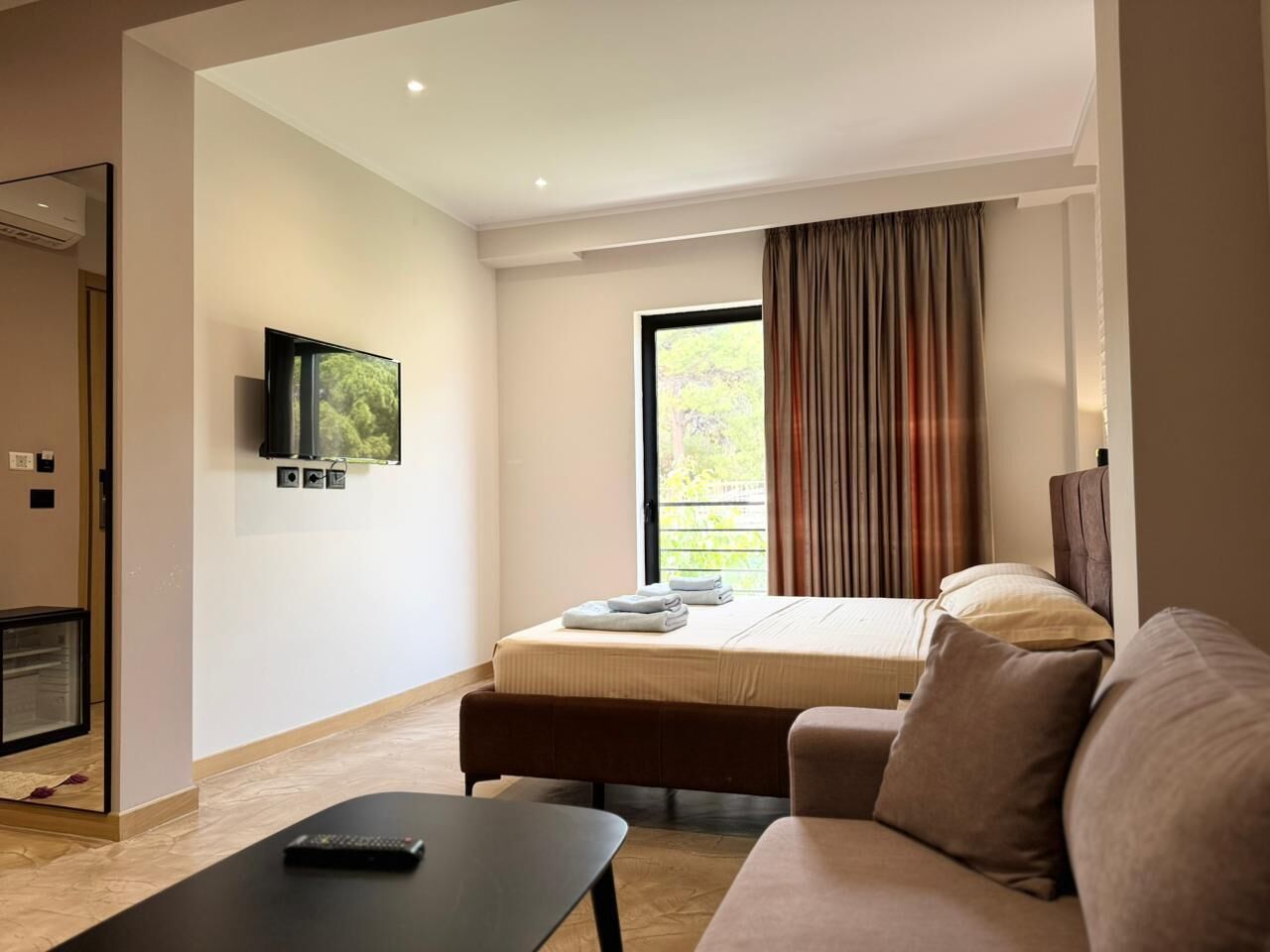 A modern hotel room with a bed, a flat-screen TV, a sofa, and a small table.