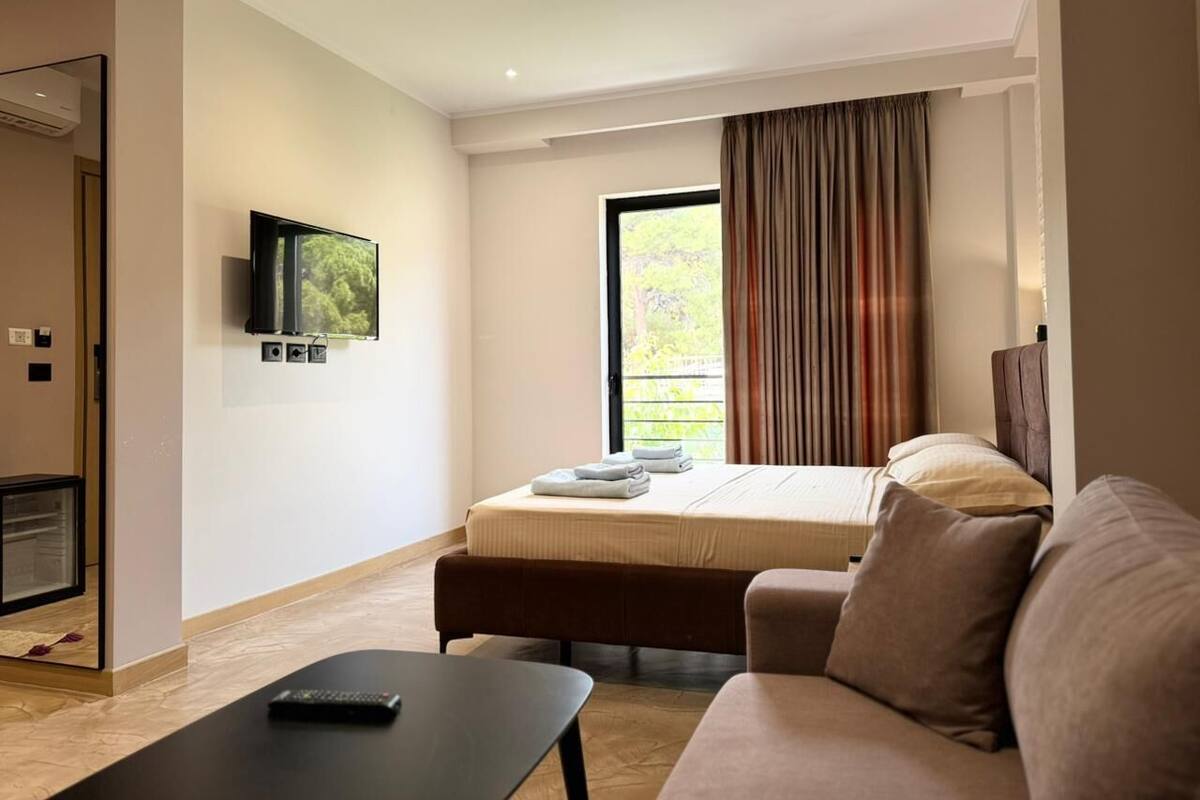 A modern hotel room with a bed, a flat-screen TV, a sofa, and a small table.