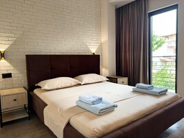 Habitación de hotel con pared de ladrillo, una cama grande con dos almohadas, dos mesitas de noche con lámparas y una ventana con cortinas.