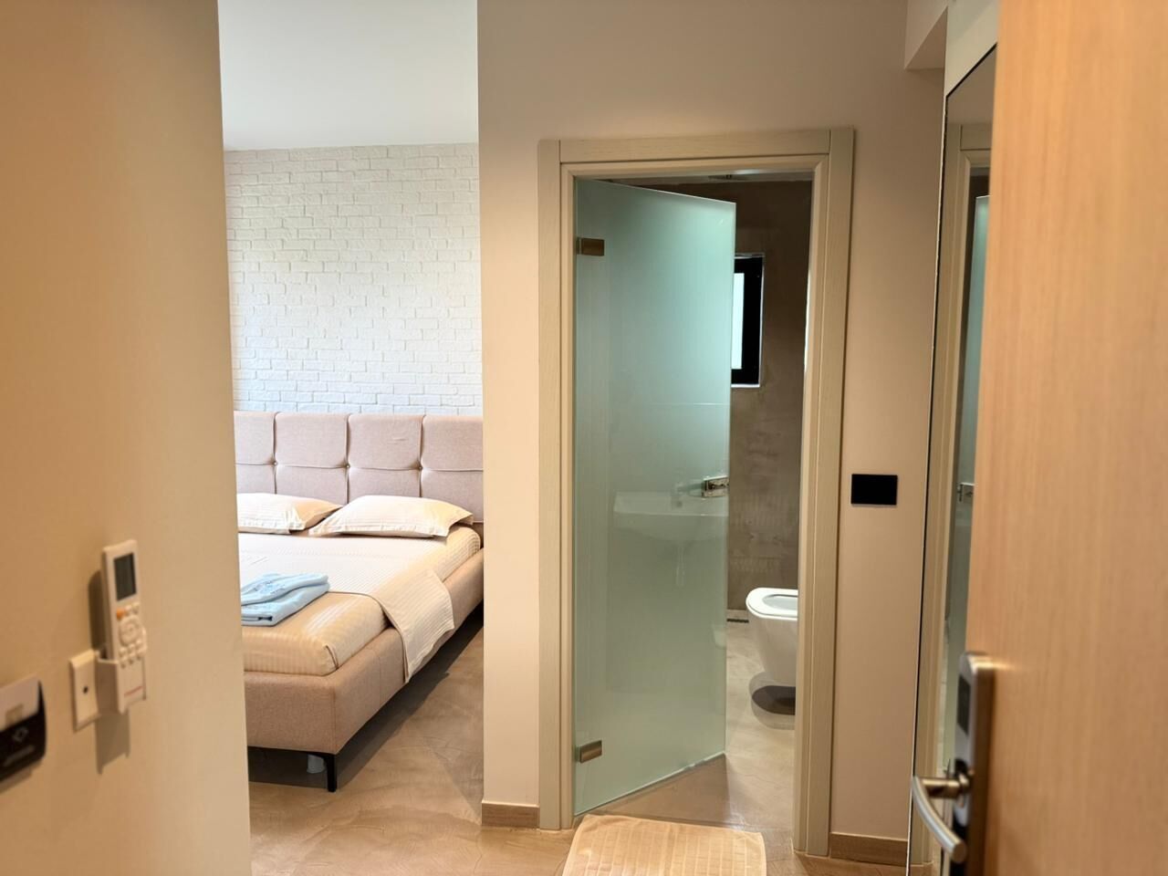 A bedroom with a bed, a bedside table, and a wall-mounted control panel.
