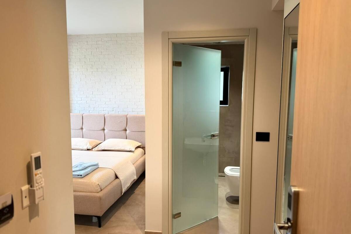 A bedroom with a bed, a bedside table, and a wall-mounted control panel.