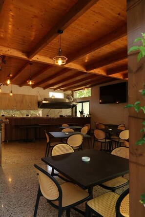 A restaurant with wooden ceiling beams, a kitchen area, and seating with woven chairs. - Ritson Hotel  (Qender Vlore)