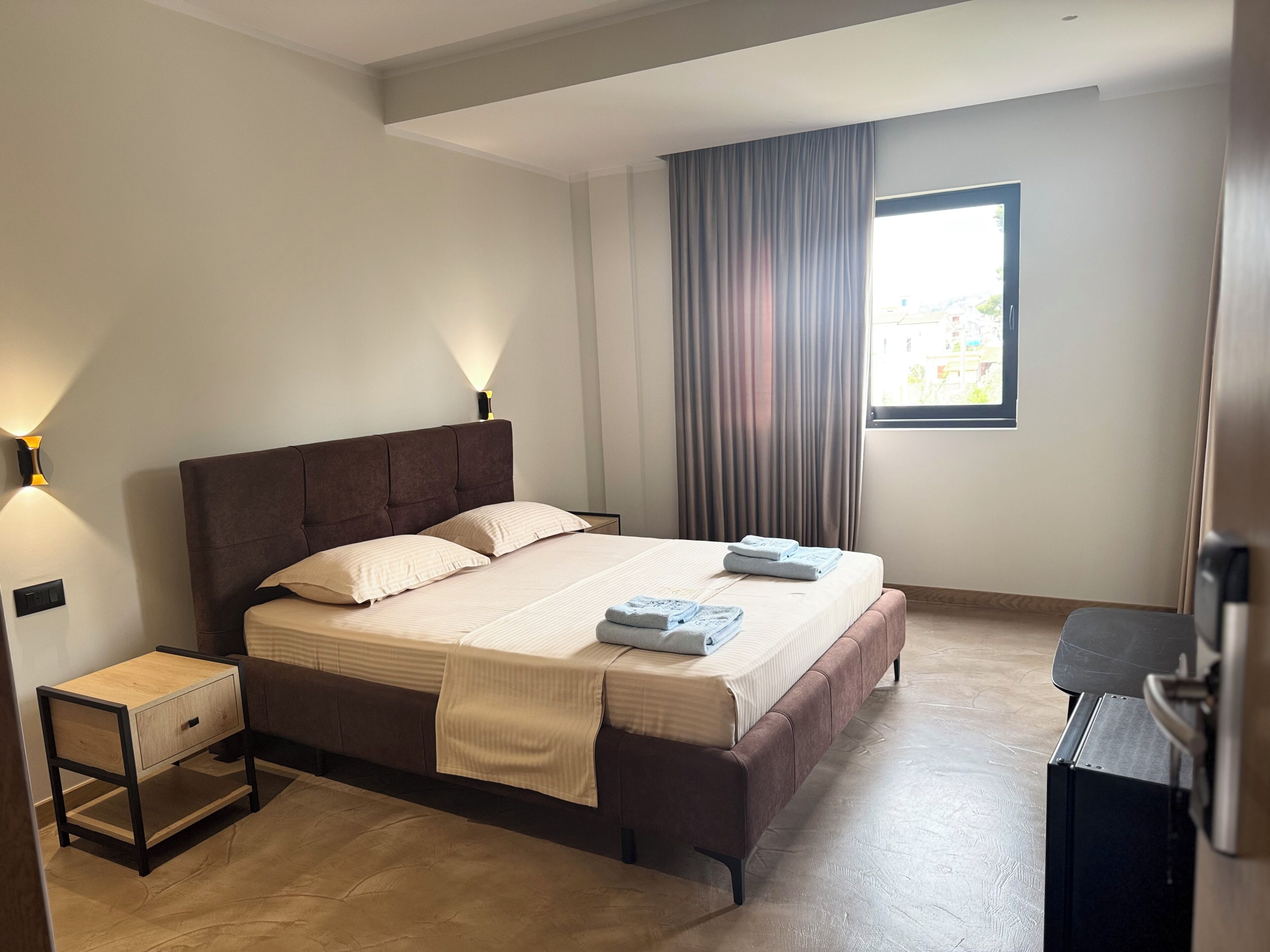 A neatly arranged bedroom with a bed, bedside tables, a desk, and a window with curtains.