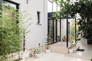 Una entrada de hotel moderna con puerta de cristal, plantas en macetas y un piso de baldosas limpias.