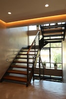 Una escalera moderna con barandilla de metal, suelo de concreto y vista a la vegetación exterior.