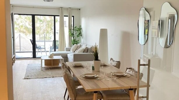 Ein Essbereich mit Holztisch, gedeckt für vier Personen, einer Couch und einem großen Spiegel an der Wand.