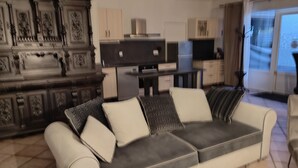 A living room with a sofa, a television, and a kitchen area in the background.