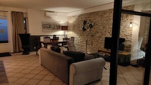 A living room with a stone wall, a sofa, a dining table with chairs, and a TV.