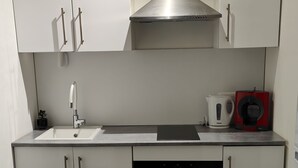 A modern kitchen with white cabinets, a stainless steel range hood, a dishwasher, an oven, and a coffee maker.