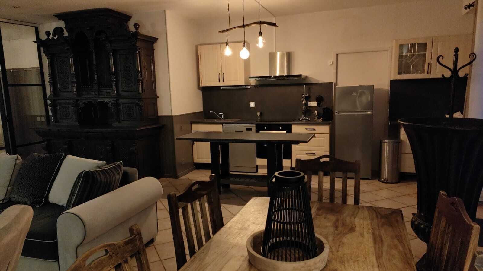 Une cuisine moderne dotée d’un îlot central, de meubles de rangement aux couleurs sombres et d’un éclairage suspendu.